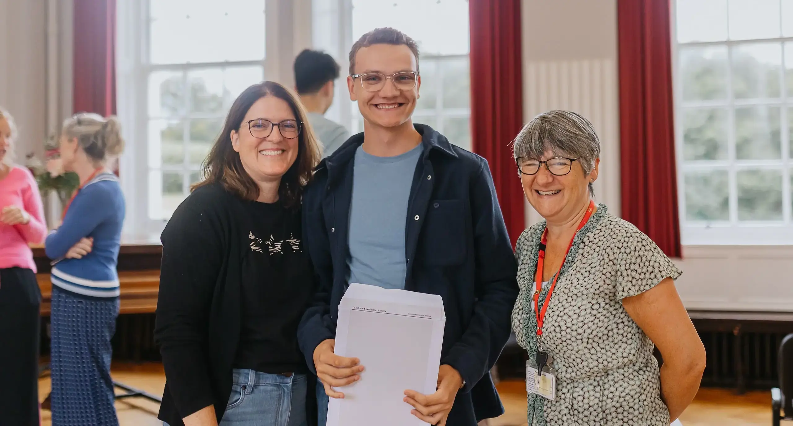 Radnor student, flanked by two teachers, smiles while holding a results envelope