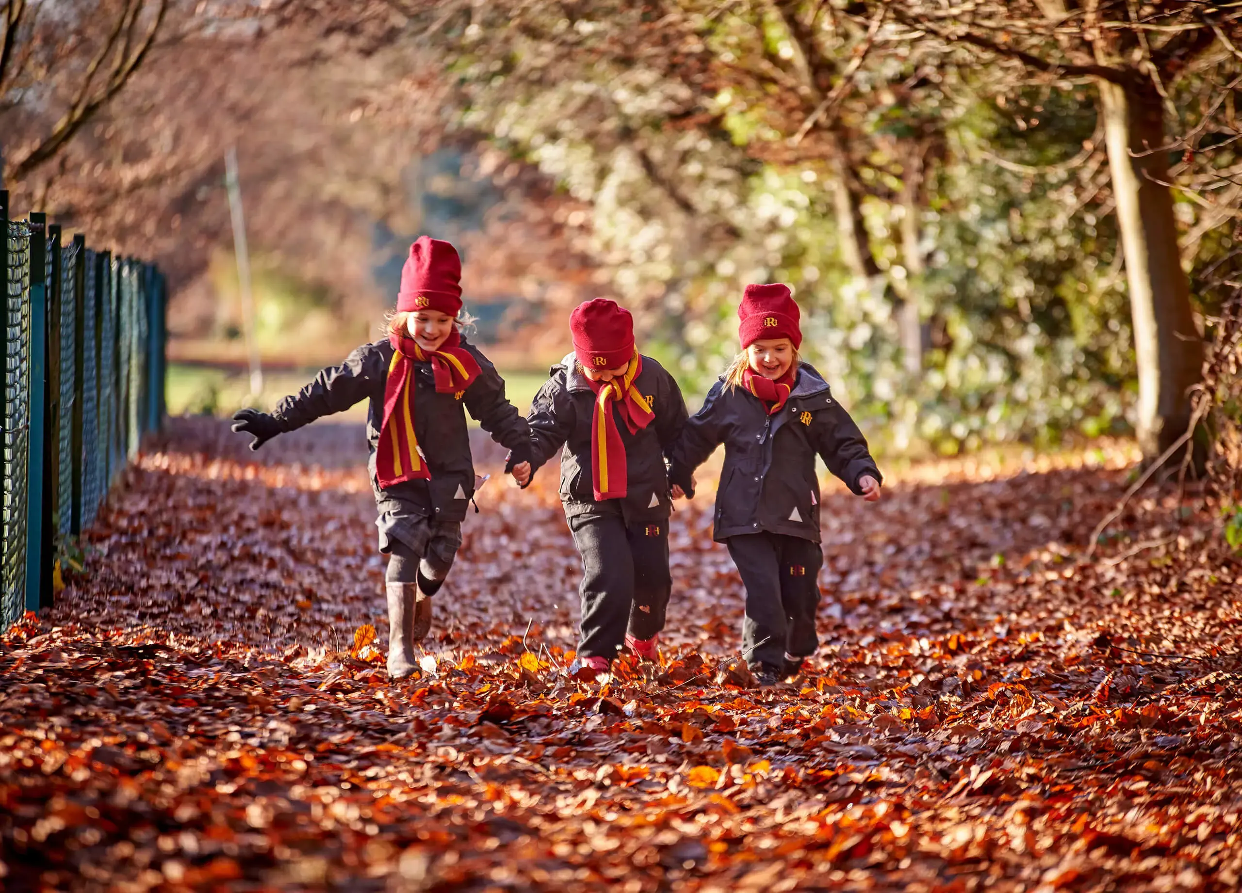 Happy Radnor House Sevenoaks pupils holding hands and running along autumnal path