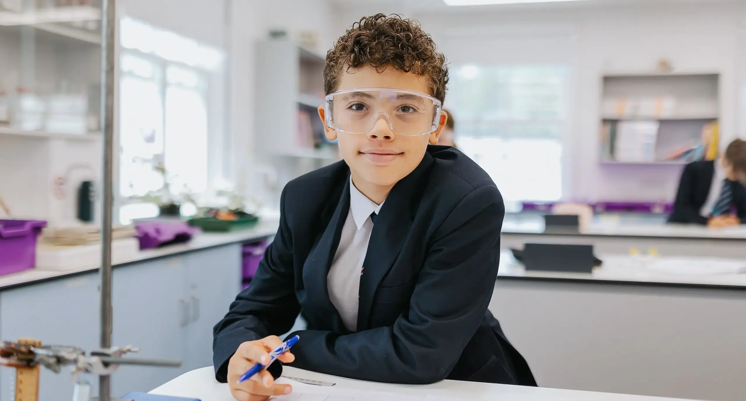 Smiling student in a science lab, wearing goggles