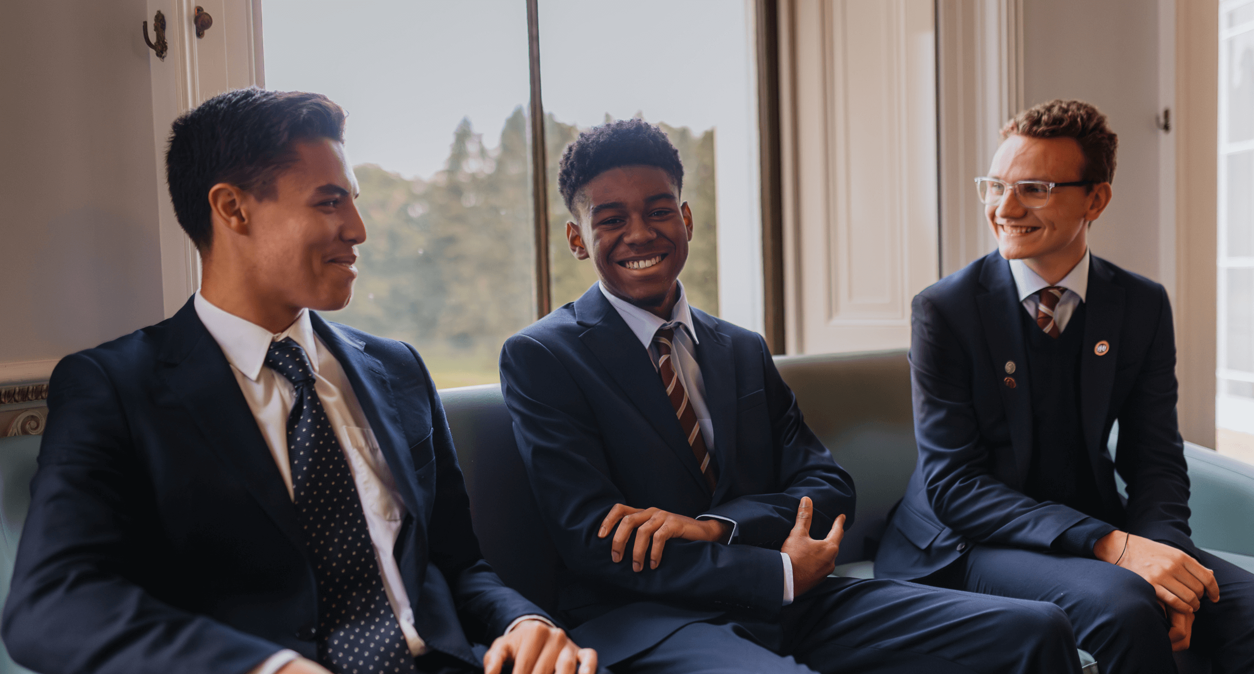 Three Sixth Formers laughing, sitting on a sofa together